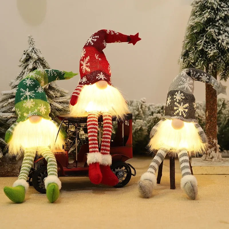 Lutins de Noël lumineux LED avec bonnets tricotés et longues jambes rayées en décor d’hiver enneigé – décoration festive chaleureuse."