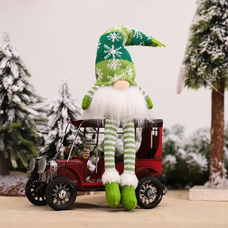 Figurine de lutin de Noël éclairée avec bonnet tricoté vert et blanc devant un sapin enneigé.