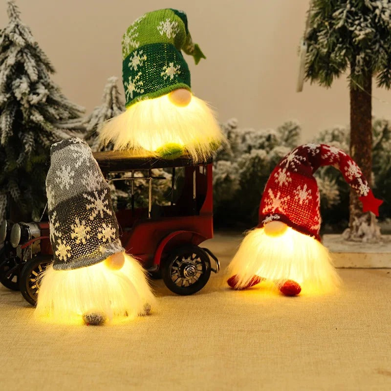 Décoration de Noël lutins lumineux avec bonnet tricoté vert, gris et rouge posés près d’un décor enneigé – figurines LED pour ambiance festive."