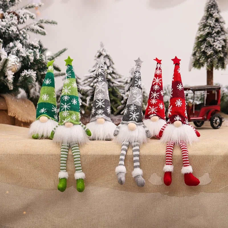 Petits lutins de Noël assis avec bonnets tricotés verts, gris et rouges et longues jambes rayées – décorations nordiques pour fêtes hivernales."