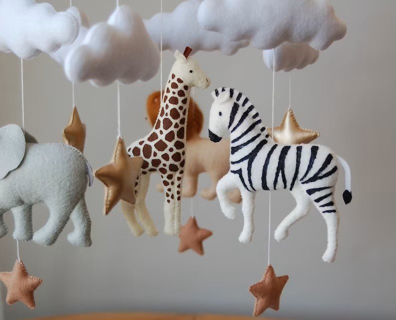 Détails des peluches du mobile Safari : éléphant gris, girafe jaune, lion doré et zèbre rayé, conçus en matières douces et naturelles.