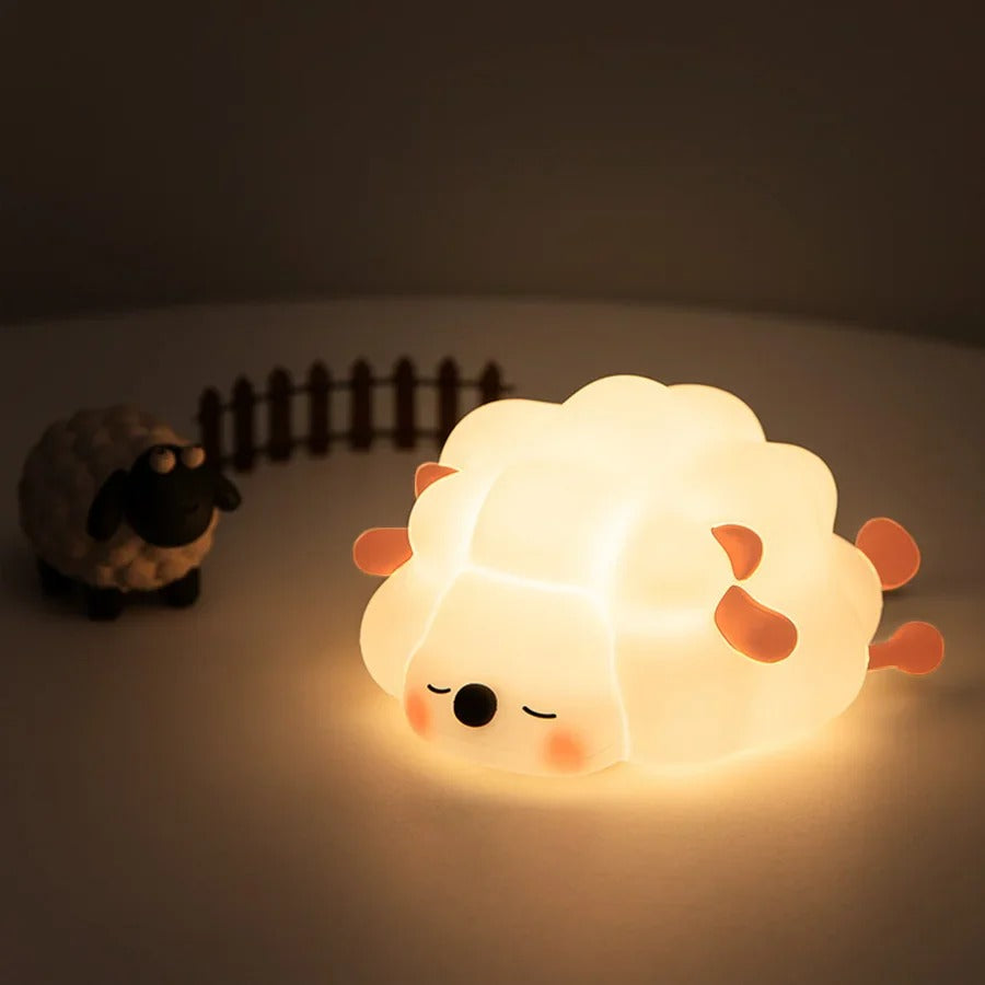 Veilleuse bébé BabyDream™ Sheep au design adorable en forme de mouton, posée sur une surface plane à côté d'une petite figurine de mouton dans une ambiance douce."