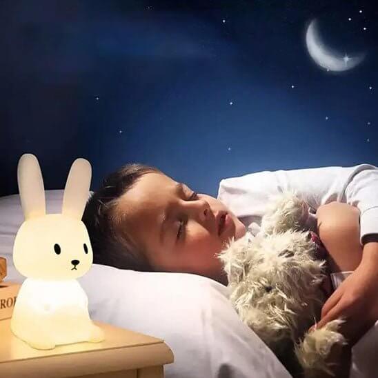 Veilleuse lapin LumiLapin allumée sur une table de nuit, créant une ambiance douce dans la chambre de bébé.