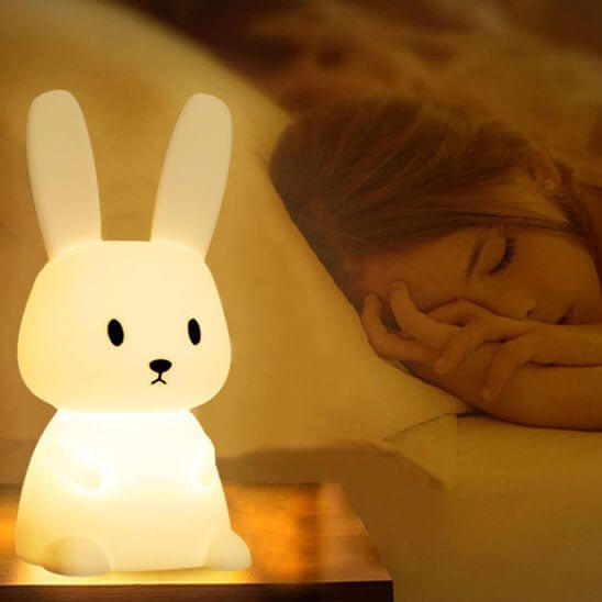 Bébé dormant paisiblement avec la veilleuse lapin LumiLapin diffusant une lumière apaisante.