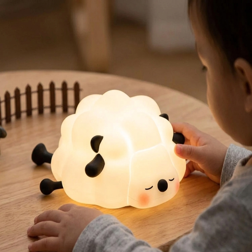 Un jeune enfant observe avec curiosité la veilleuse bébé BabyDream™ Sheep posée sur une table en bois dans une chambre calme.